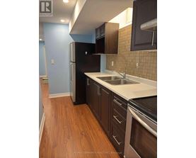 A kitchen with a black fridge and wooden floors.
