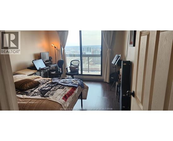A bedroom with a large bed and a balcony with a view of the city.