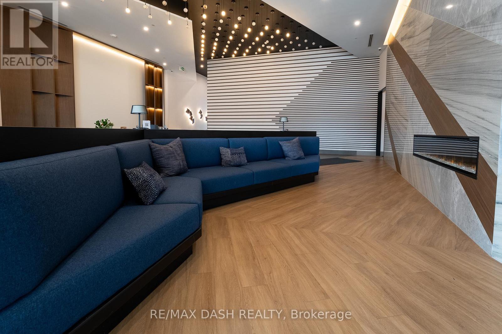 A blue couch sits in a spacious room with wooden flooring and a staircase on the right side.