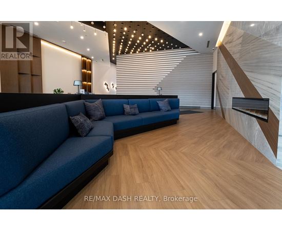 A blue couch sits in a spacious room with wooden flooring and a staircase on the right side.