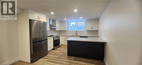 A kitchen with a black refrigerator and wooden floors.