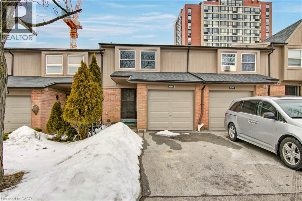A grey car is parked in front of a two-story house with a garage.
