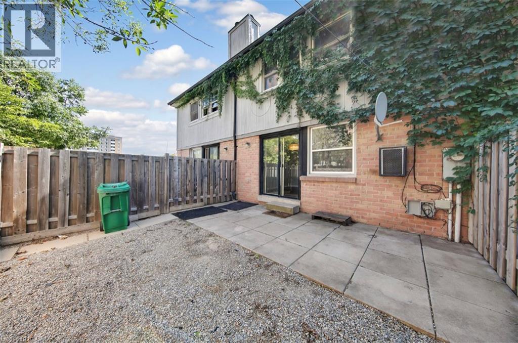 A backyard with a gravel area, a wooden fence, and a building with a green trash can.