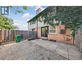 A backyard with a gravel area, a wooden fence, and a building with a green trash can.