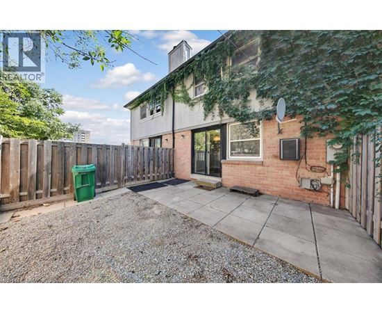 A backyard with a gravel area, a wooden fence, and a building with a green trash can.