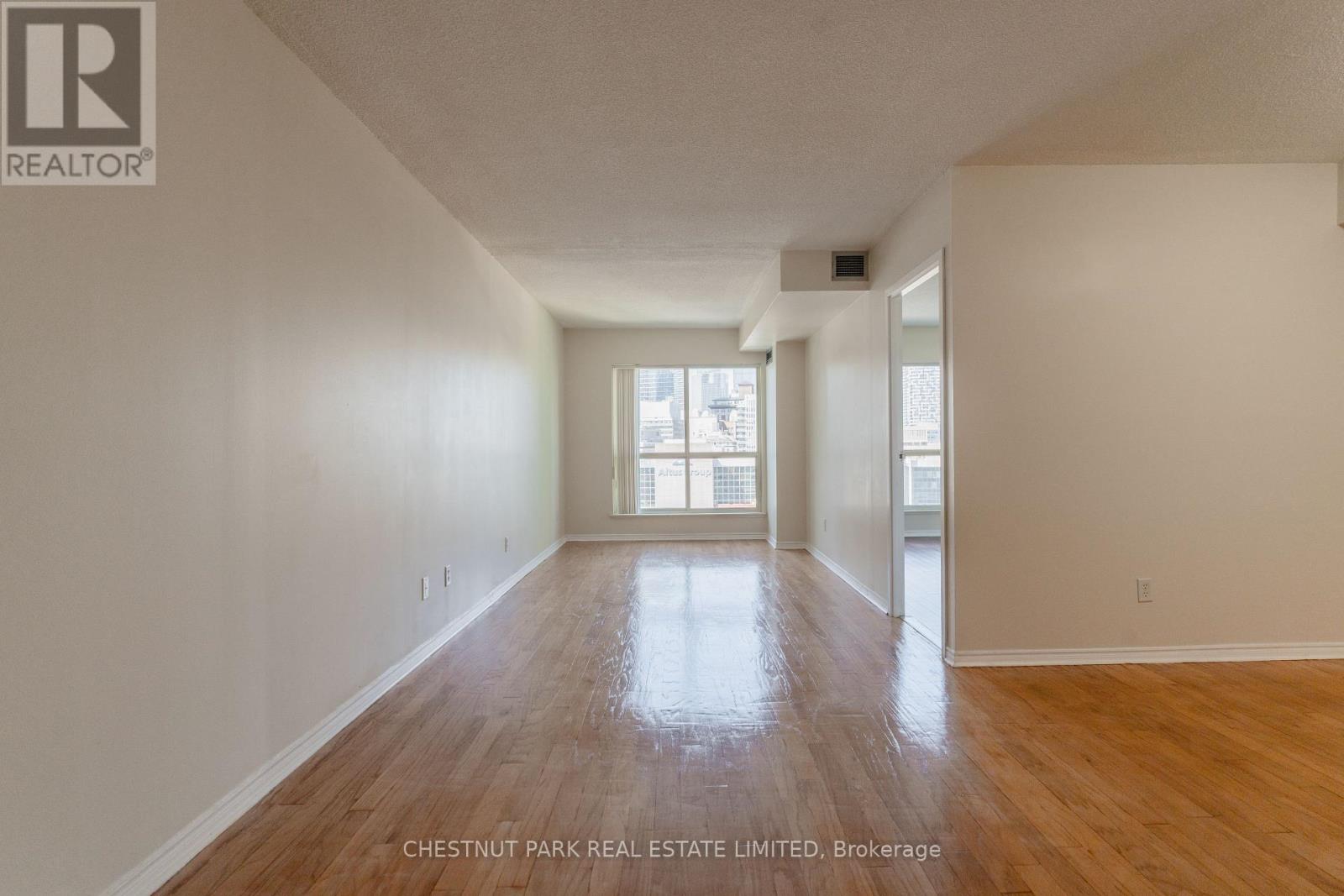 A spacious room with wood flooring and a large window.