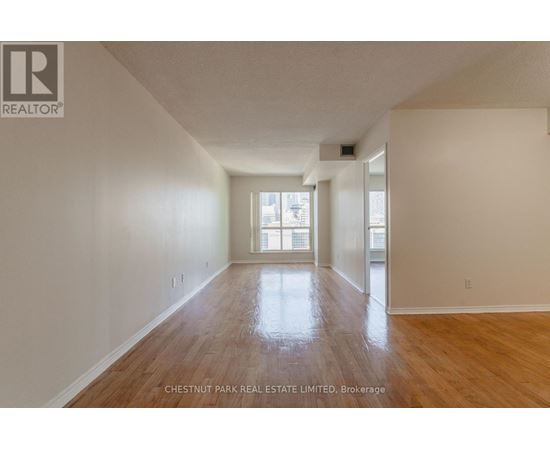 A spacious room with wood flooring and a large window.
