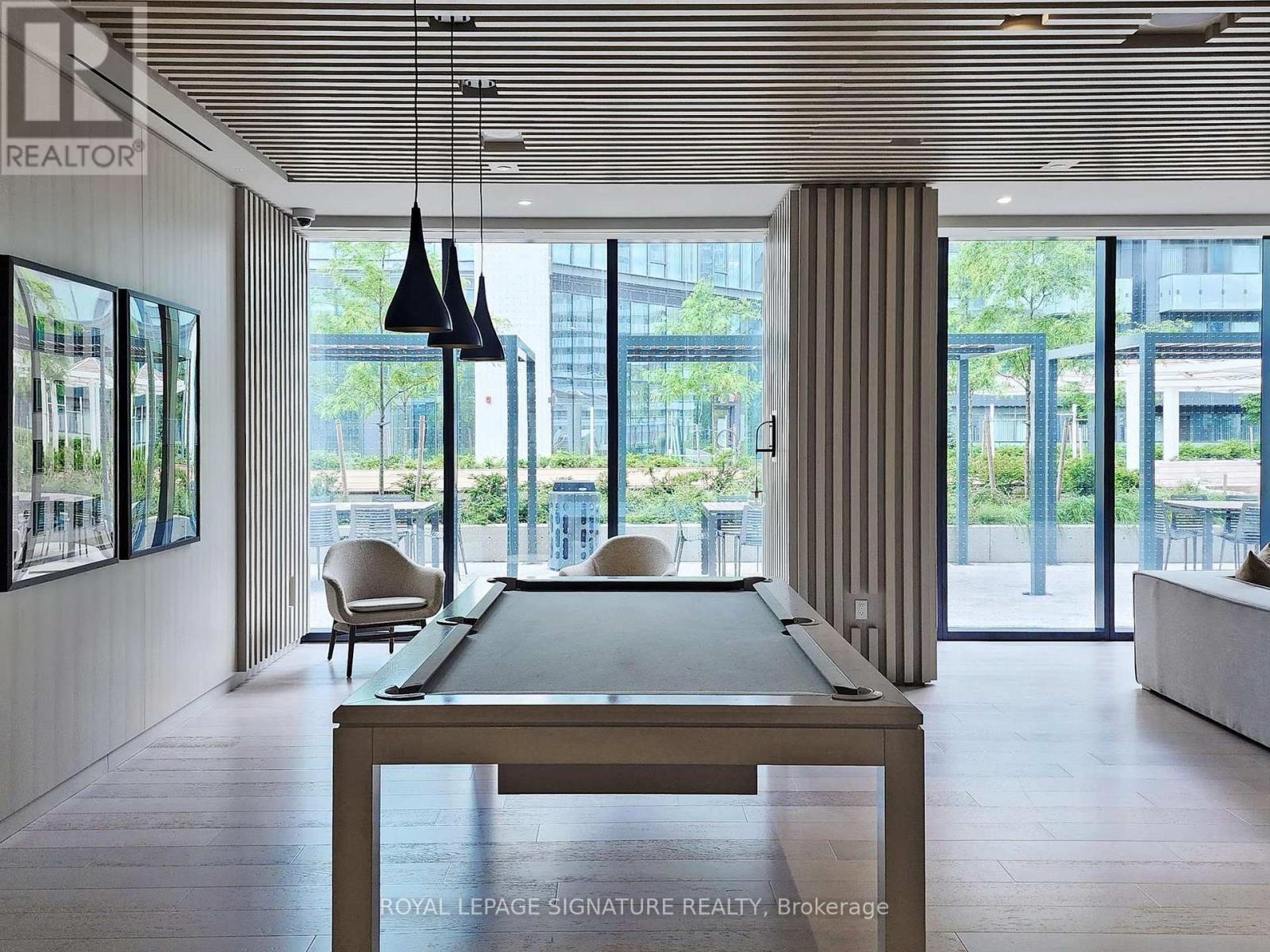 A billiard table is in the middle of a room with a pool table chair and a hanging light.