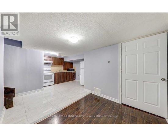 A spacious room with a white door and a kitchen area in the background.