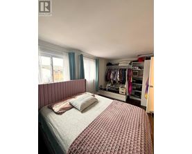 A bedroom with a bed, a window with blue curtains, and a wardrobe with clothes.