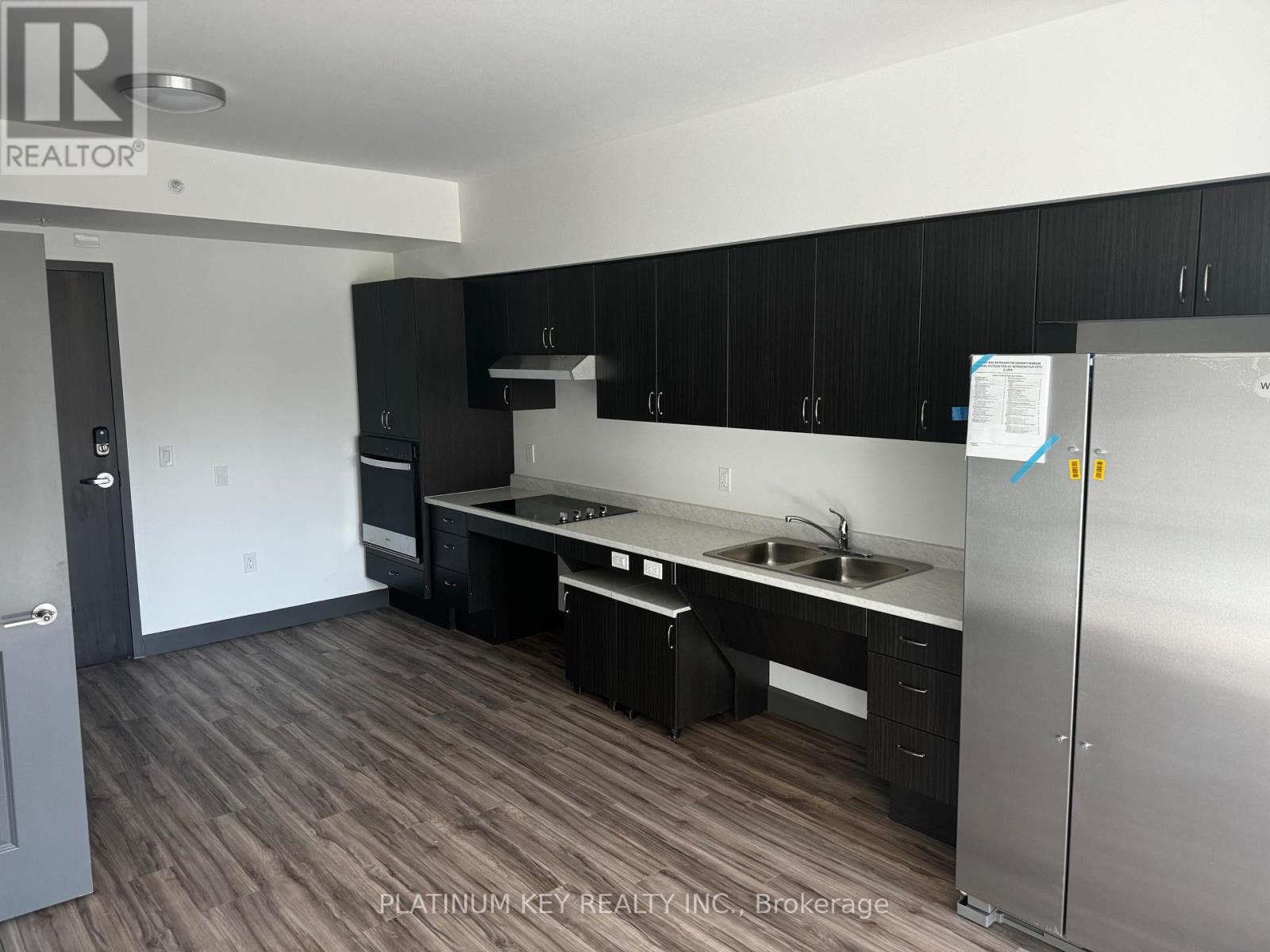 A kitchen with black cabinets and a stainless steel refrigerator.