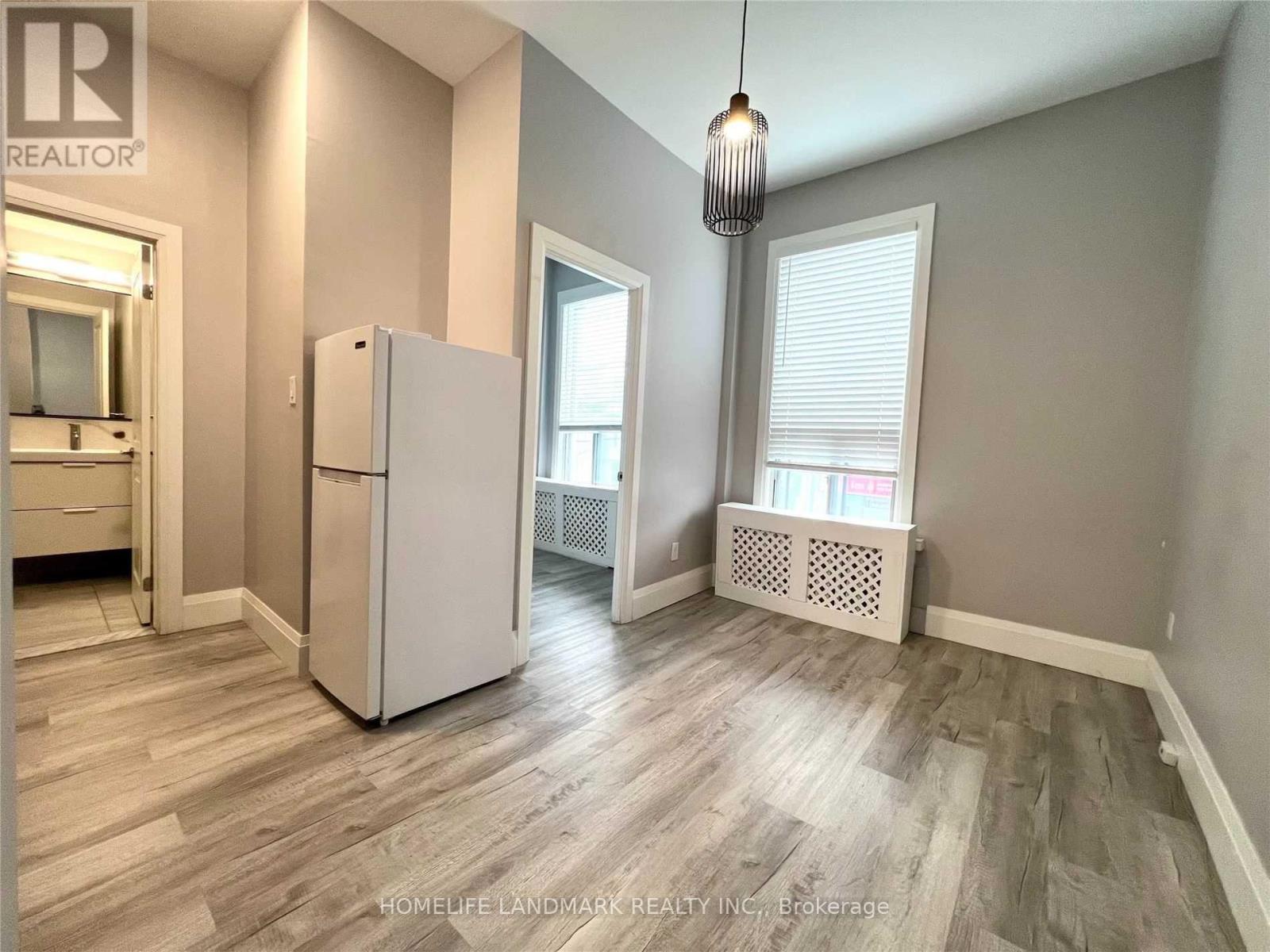 A room with a white refrigerator and wooden flooring.