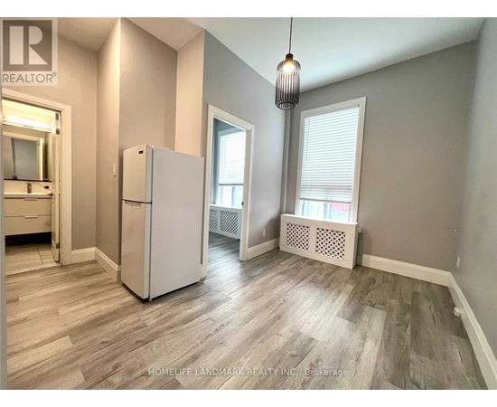 A room with a white refrigerator and wooden flooring.