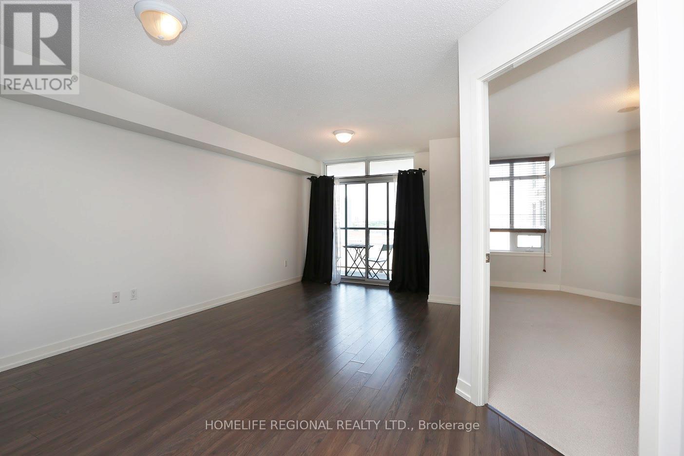 A spacious room with wooden flooring and white walls, with a window and a door visible.