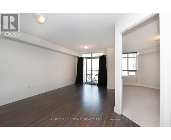 A spacious room with wooden flooring and white walls, with a window and a door visible.