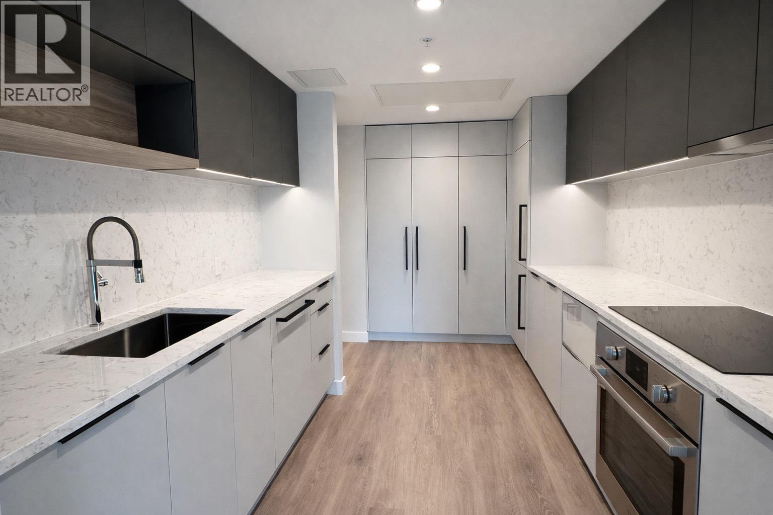 A modern kitchen with a sink, cabinets, and a stove top oven.