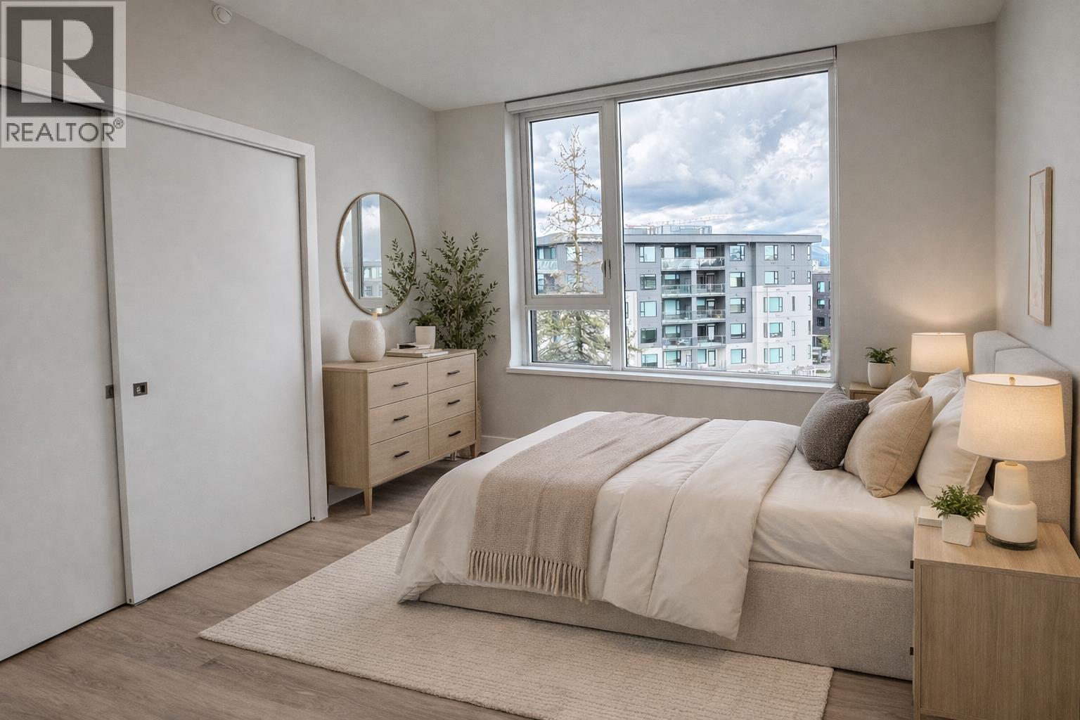 A bedroom with a large bed, a dresser, and a window overlooking a cityscape.