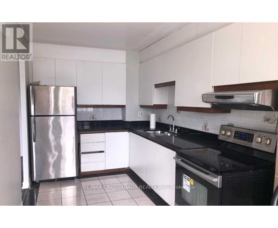 A kitchen with a stainless steel refrigerator and black countertops.
