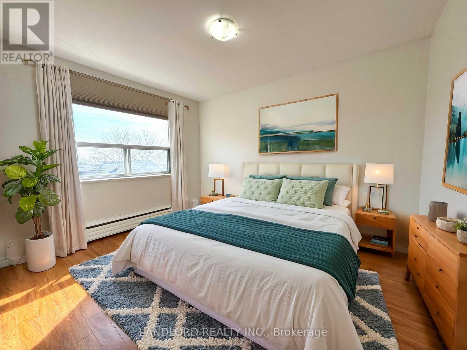 A bedroom with a large bed, a potted plant, and a painting on the wall.