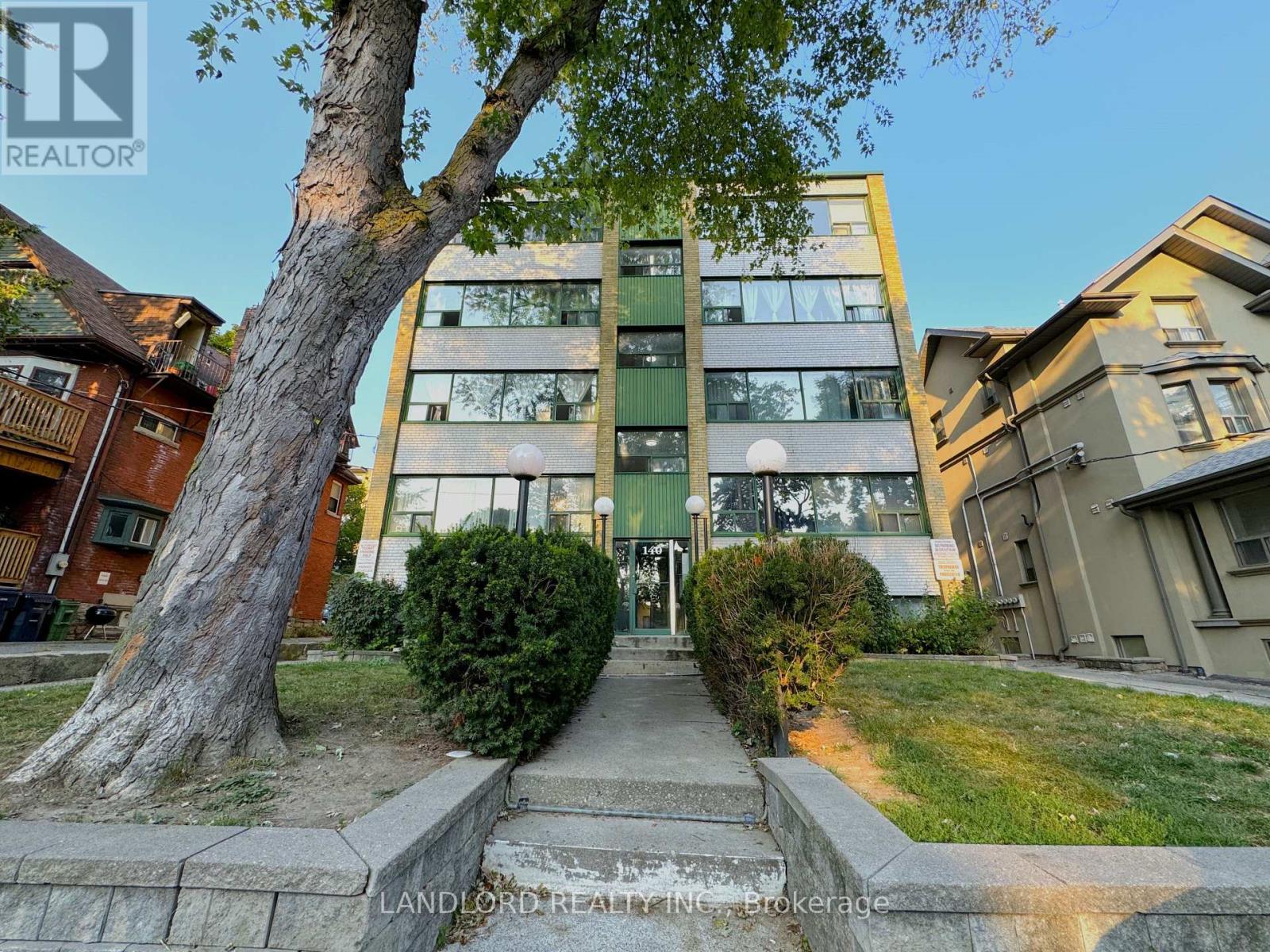 A tree stands in front of a building with a sign that says "LANDLORD REALTOR".