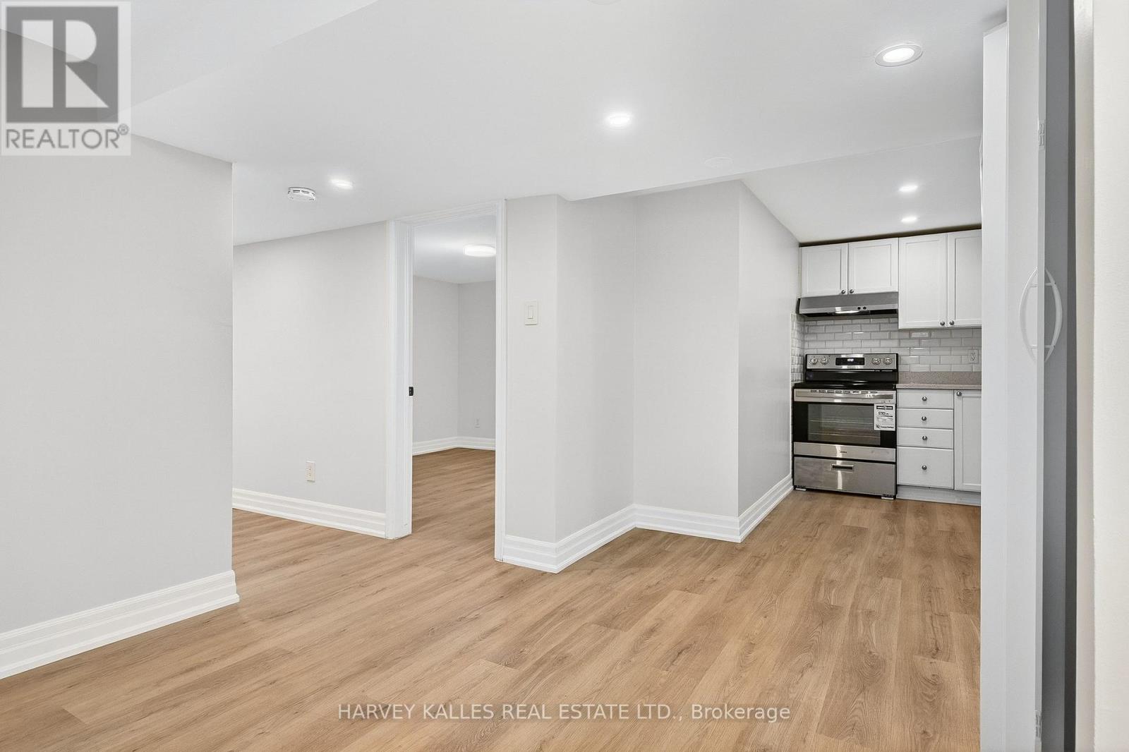 A spacious room with wooden flooring and white walls, furnished with a kitchenette.
