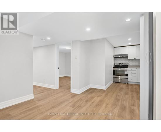 A spacious room with wooden flooring and white walls, furnished with a kitchenette.
