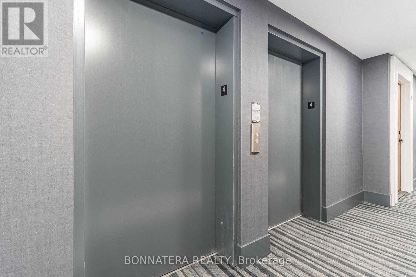 A hallway with two elevators and a brokerage sign.