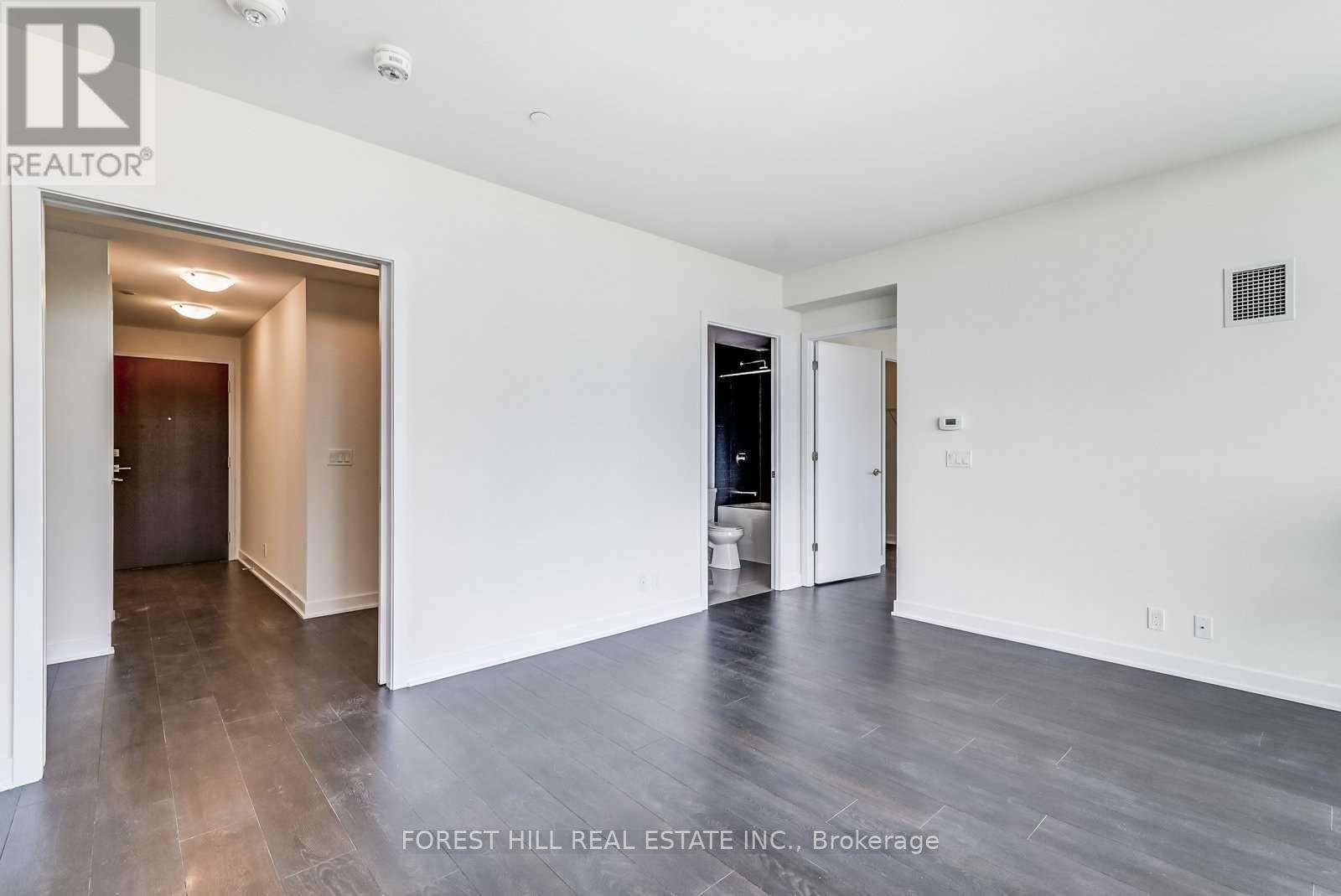A spacious room with wood flooring and white walls, with a doorway leading to another room.
