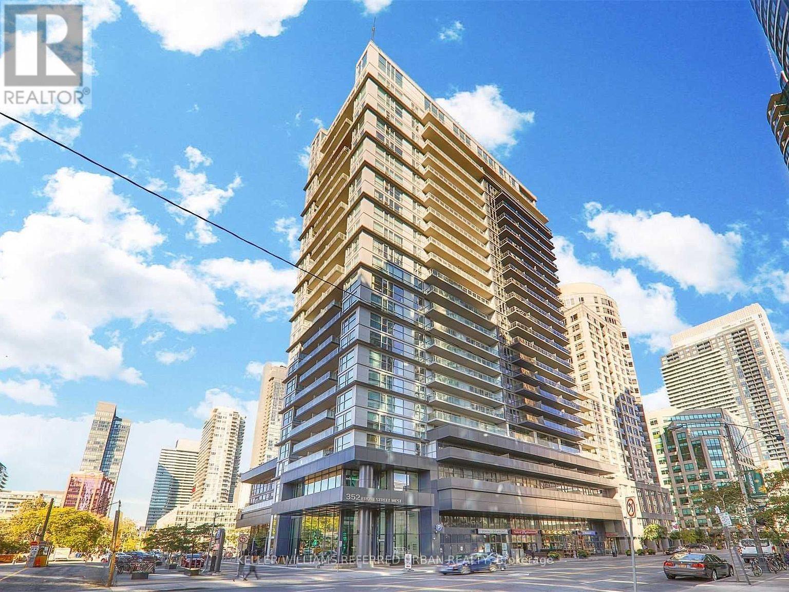 A tall building with a glass facade stands in the middle of a city street.