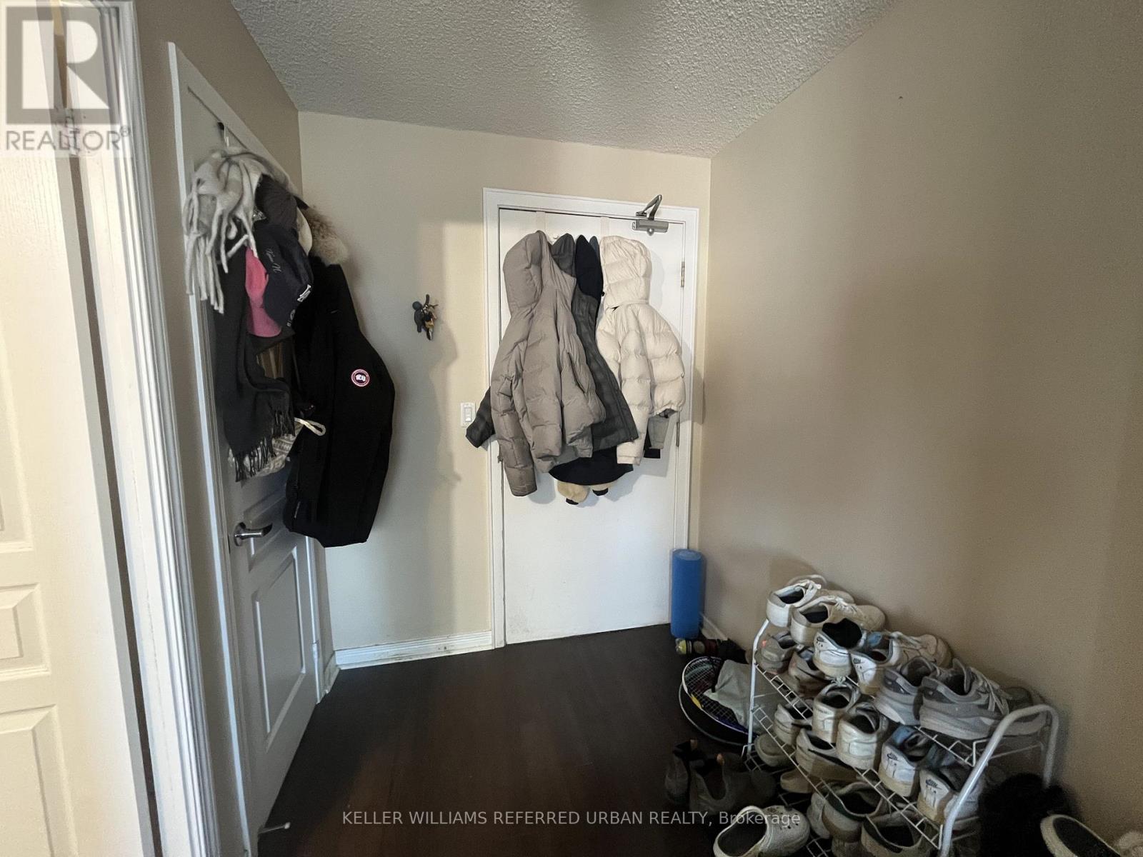 A hallway with a coat hanging on the wall and a rack of shoes on the floor.