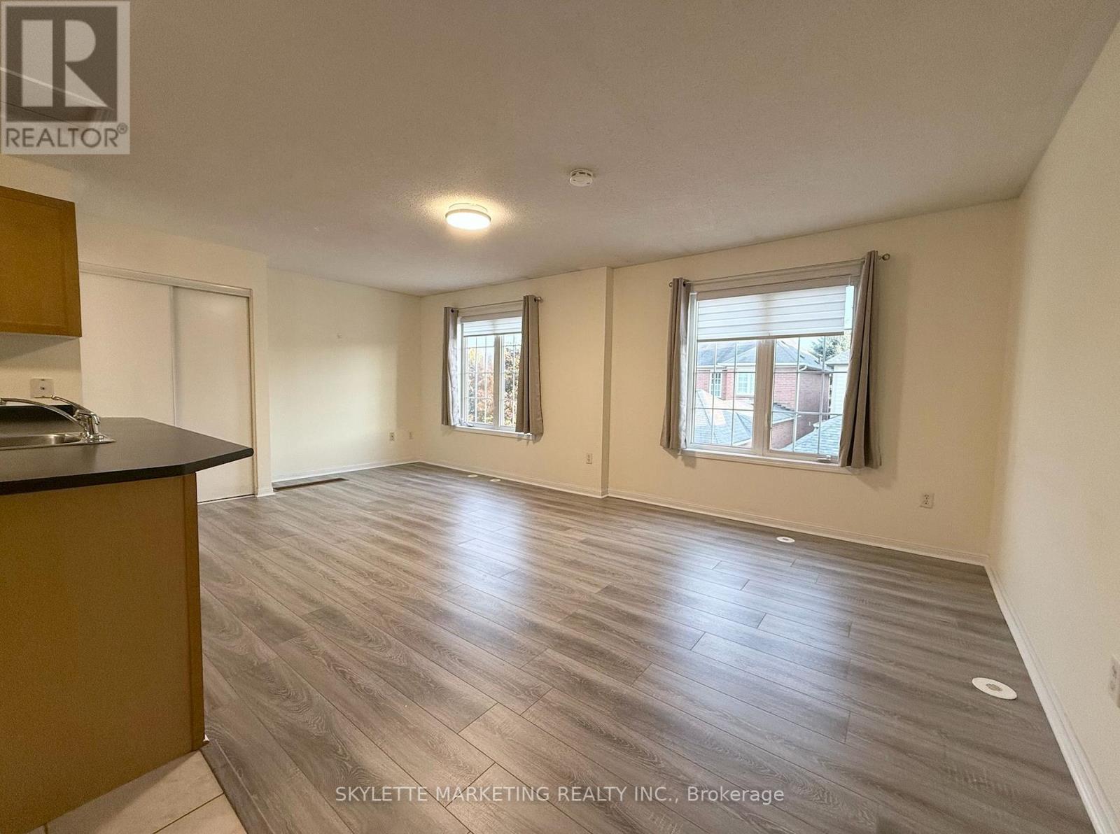 A spacious room with wooden flooring and two windows.