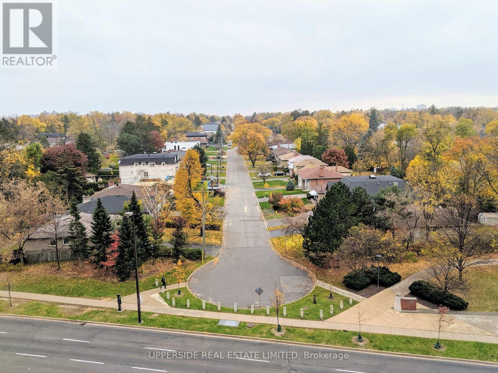 A residential street with houses on both sides and trees with autumn leaves.