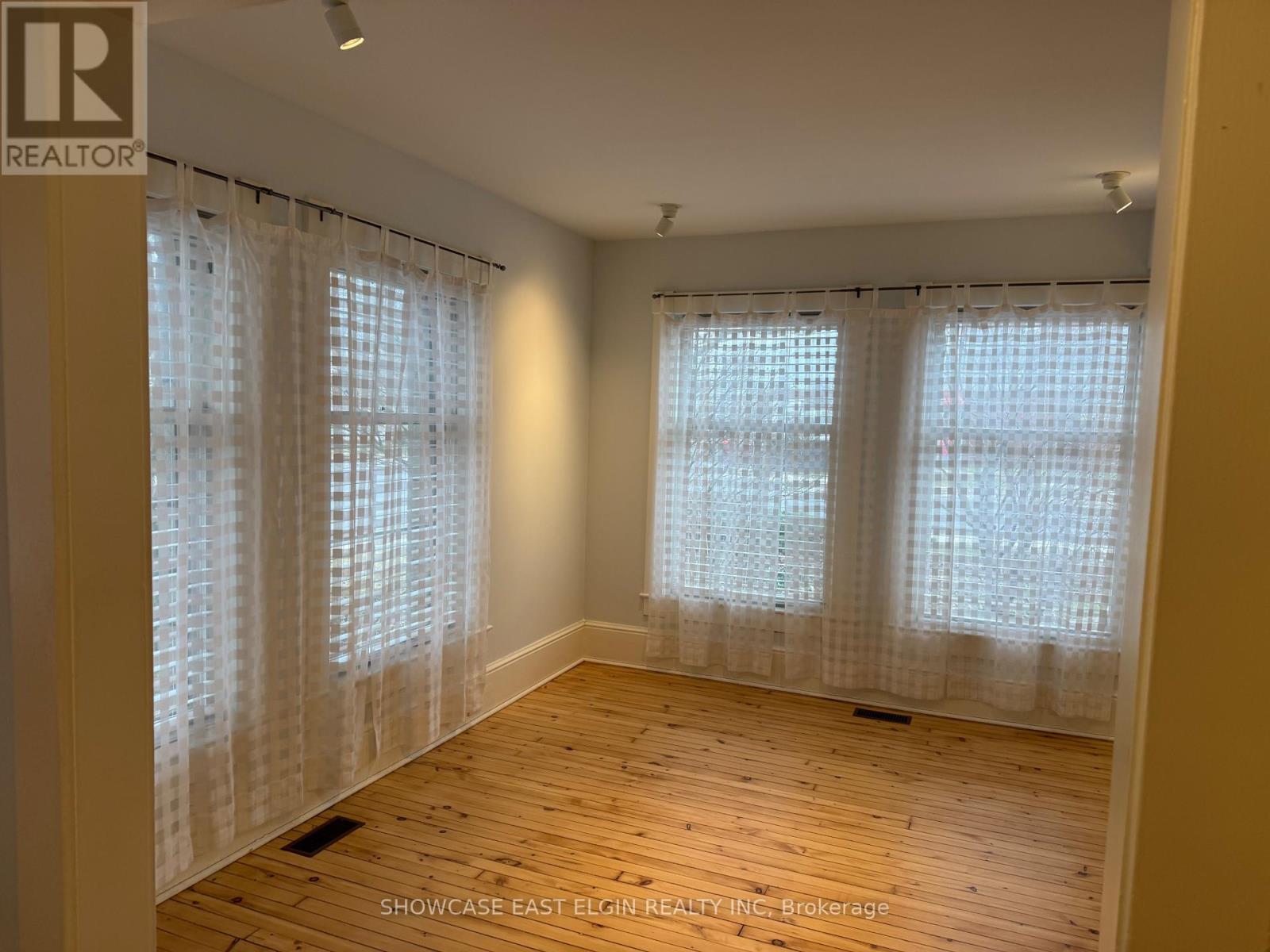A room with wooden floors and two windows covered with white curtains.