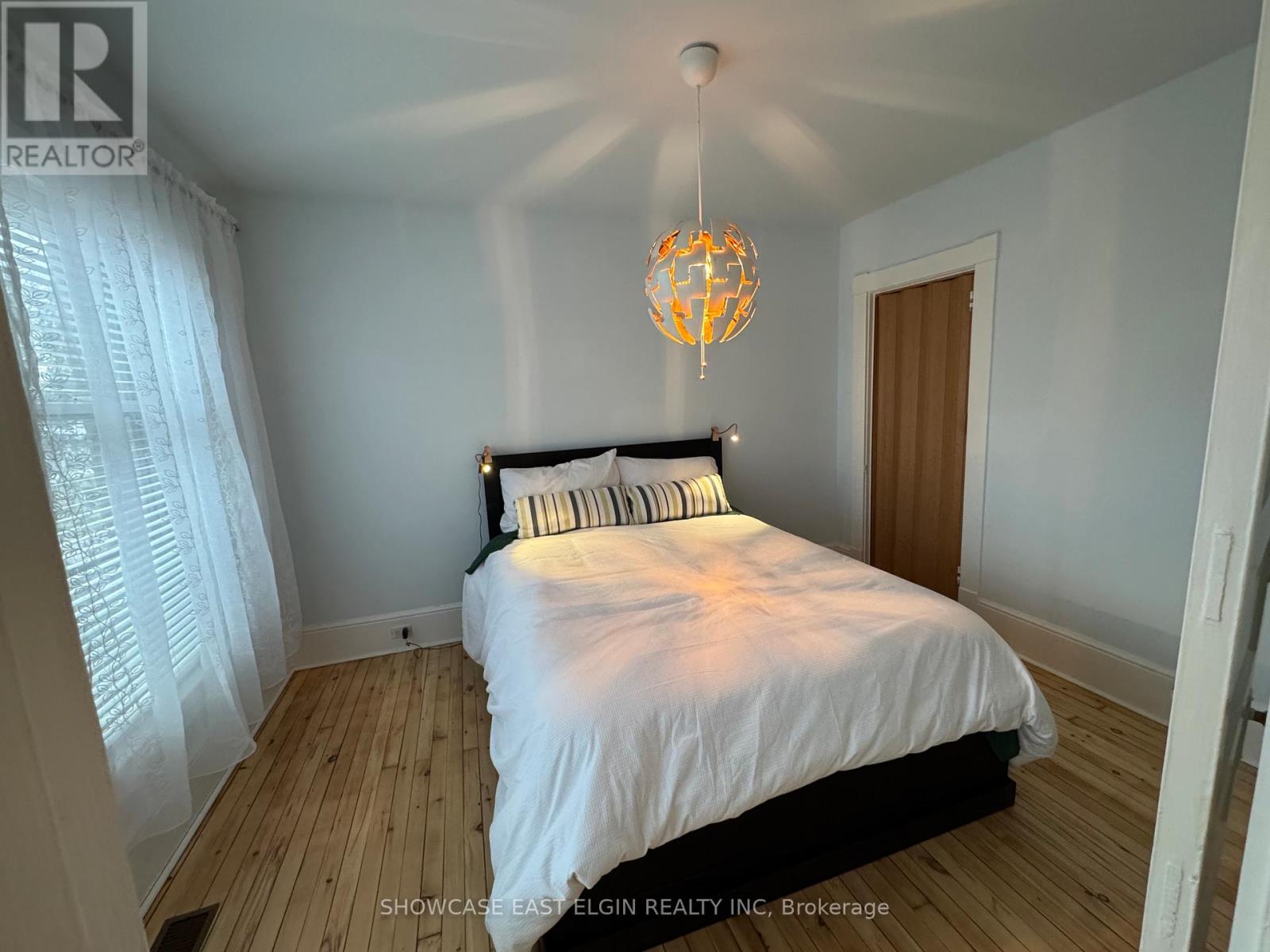 A bedroom with a bed, a chandelier, and a window with curtains.