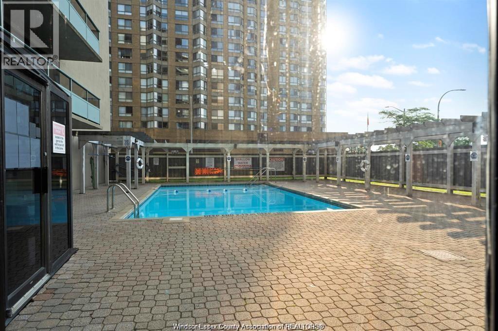 A pool surrounded by a brick patio and a fence.
