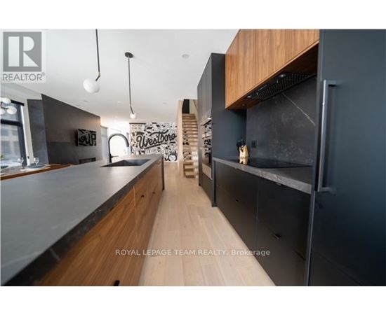 A modern kitchen with wooden cabinets and a staircase in the background.