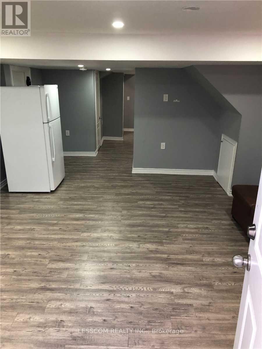 A room with a white fridge and wooden flooring.
