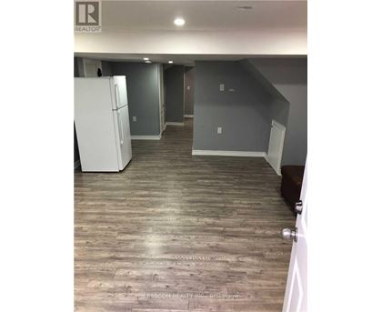 A room with a white fridge and wooden flooring.