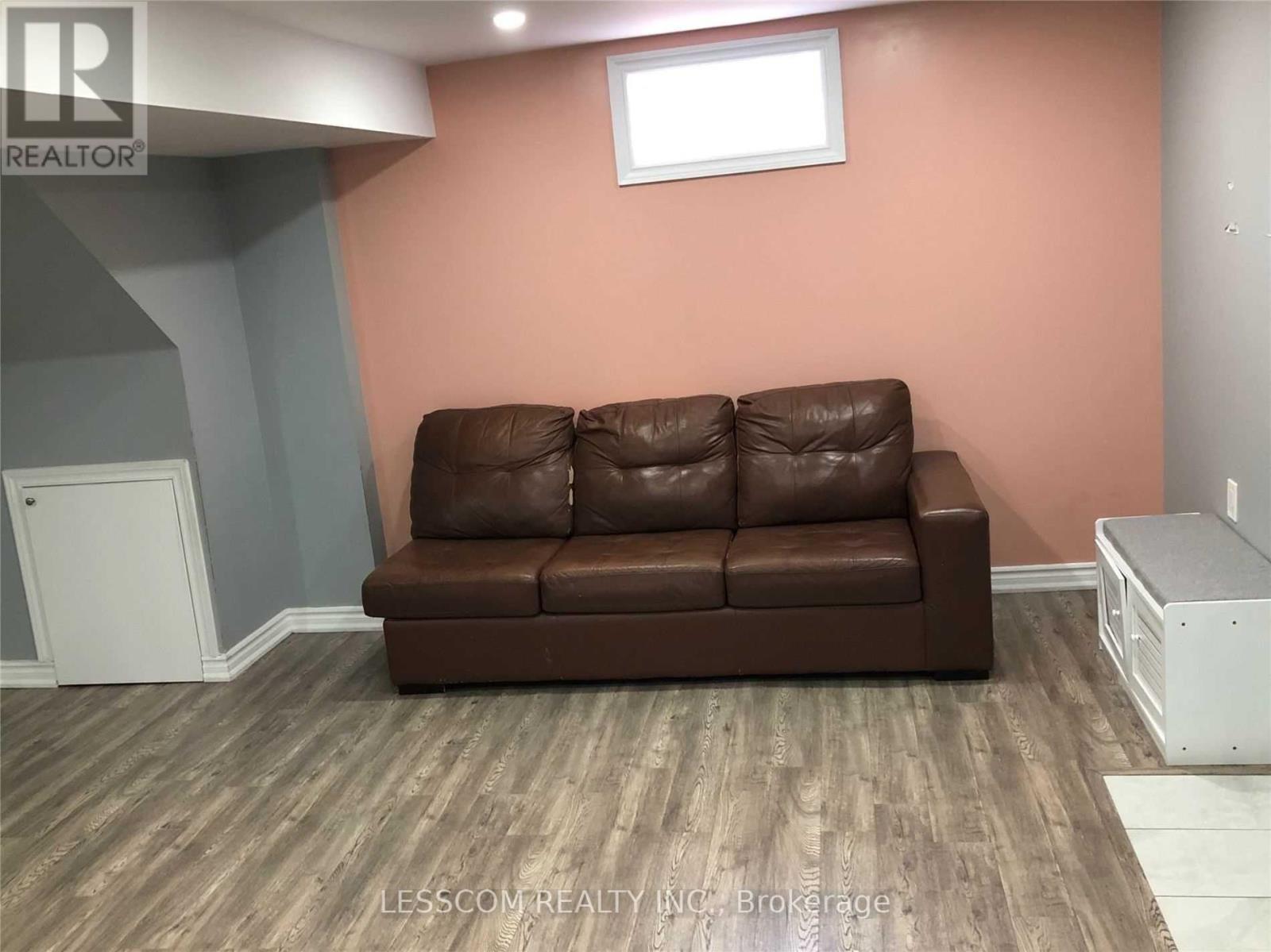 A brown leather couch sits in a room with wooden flooring and a white cabinet.