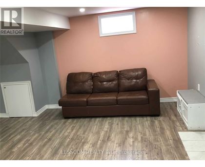 A brown leather couch sits in a room with wooden flooring and a white cabinet.