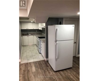 A white refrigerator stands in a kitchen with wooden floors and white cabinets.