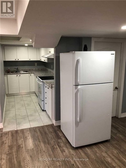 A white refrigerator stands in a kitchen with wooden floors and white cabinets.