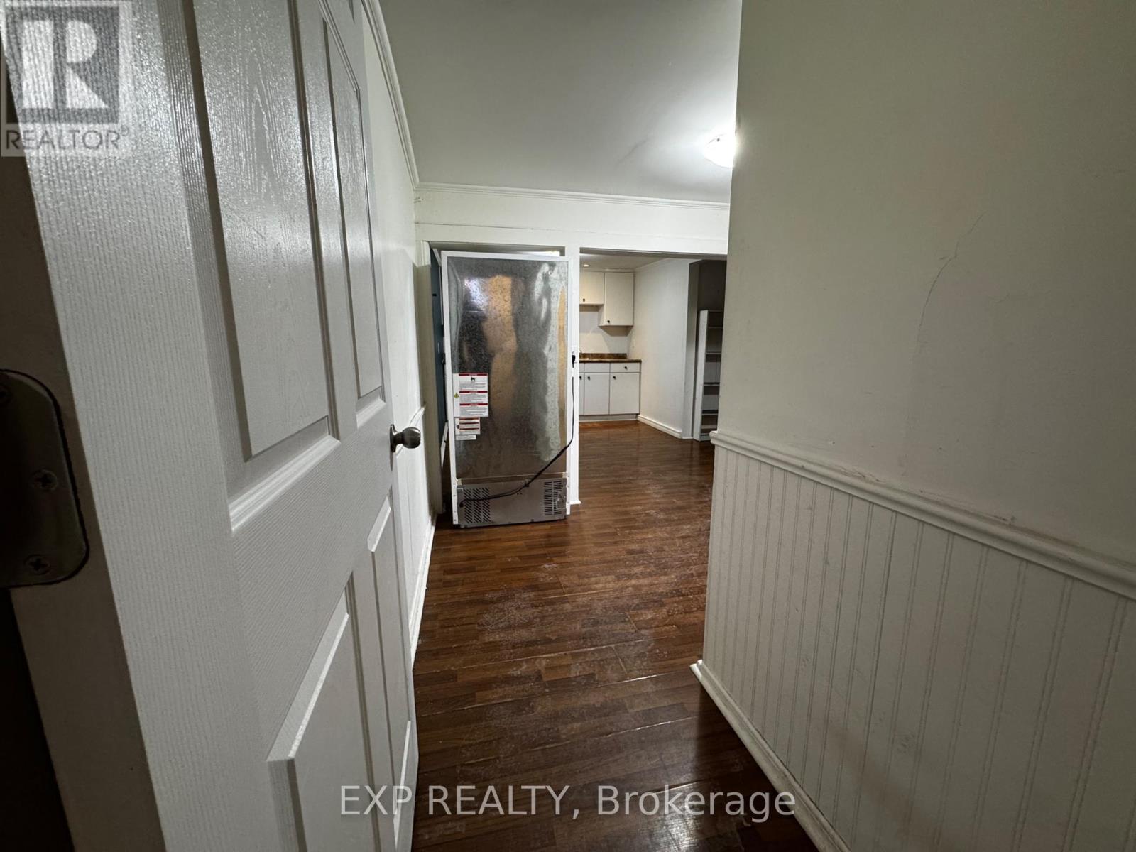 A hallway with wood floors and white walls leading to a kitchen.