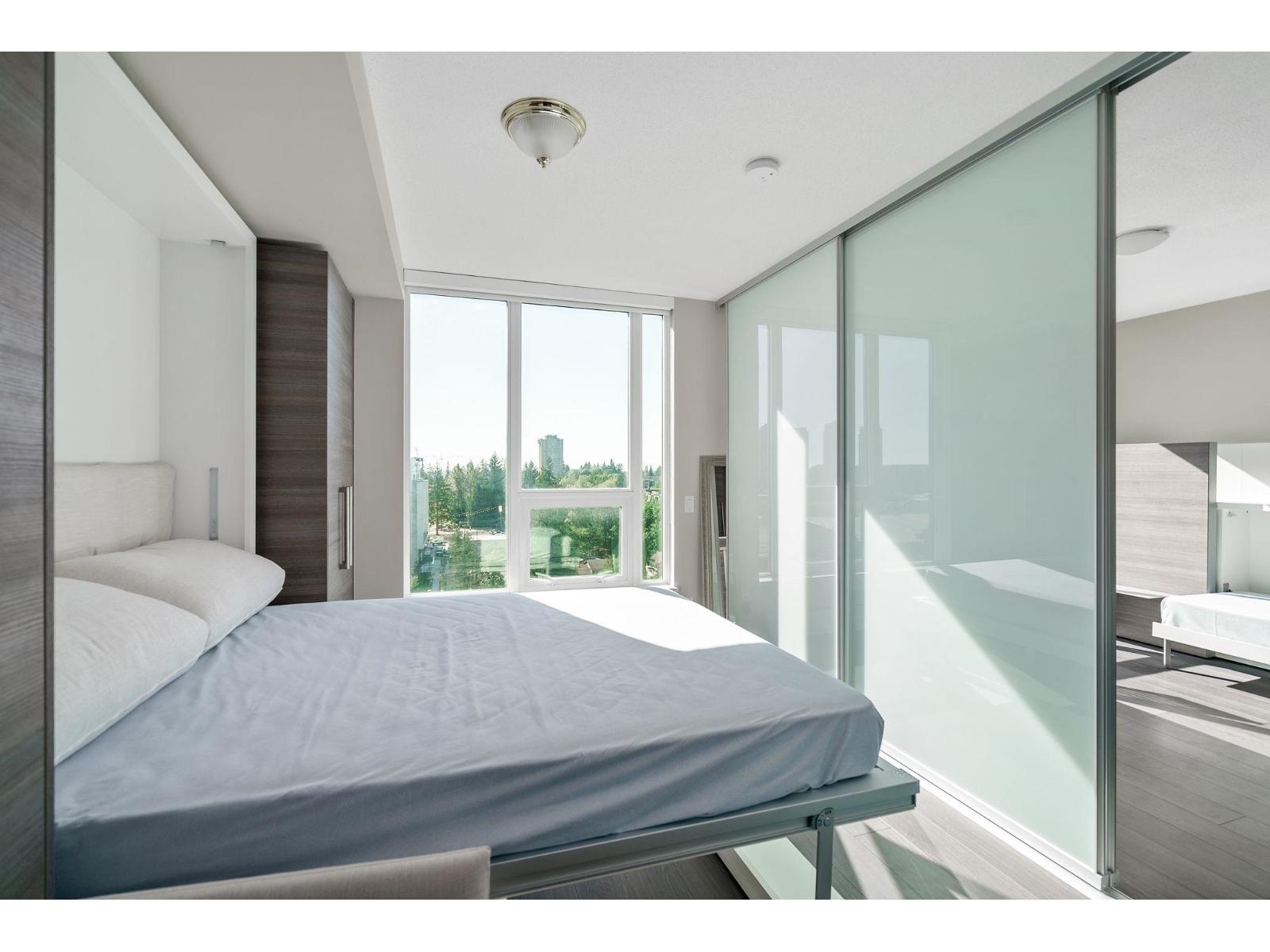 A bedroom with a large bed and a view of the outdoors through the glass doors.