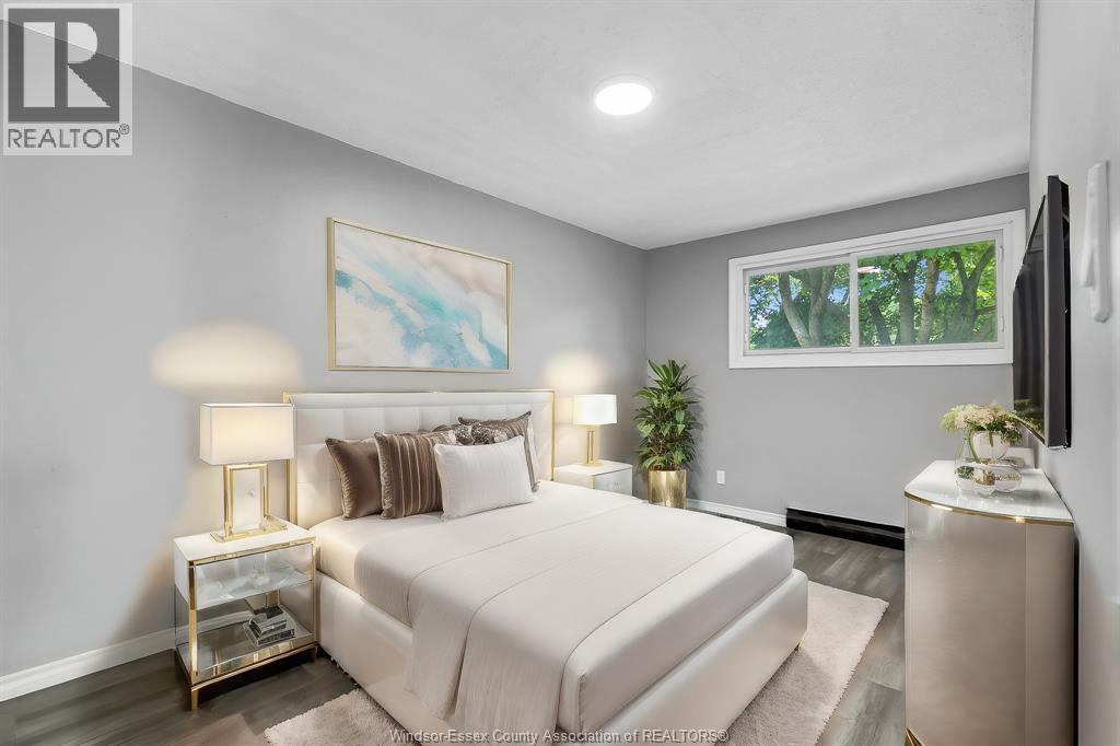 A bedroom with a large bed, a painting on the wall, and a window with a view of trees outside.