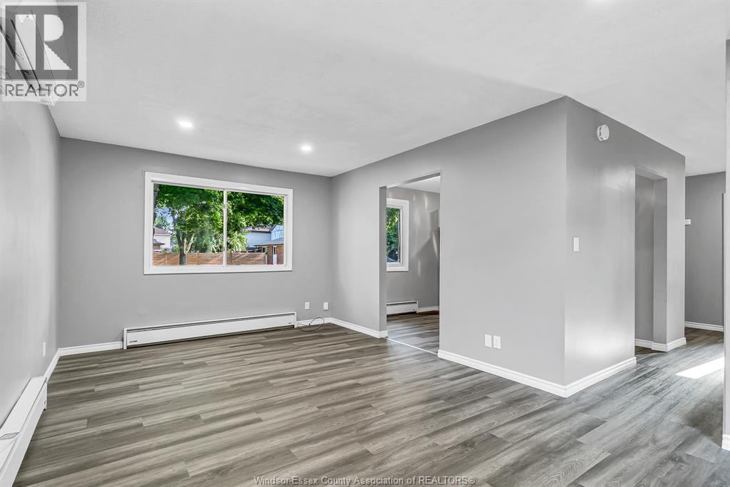 A spacious room with wooden flooring and a large window showing an outdoor view.