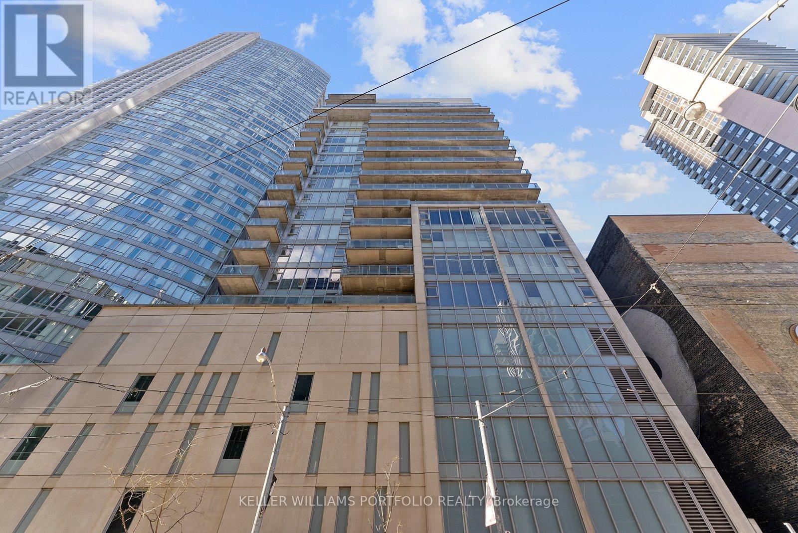 A tall building with a glass facade stands between two other buildings.