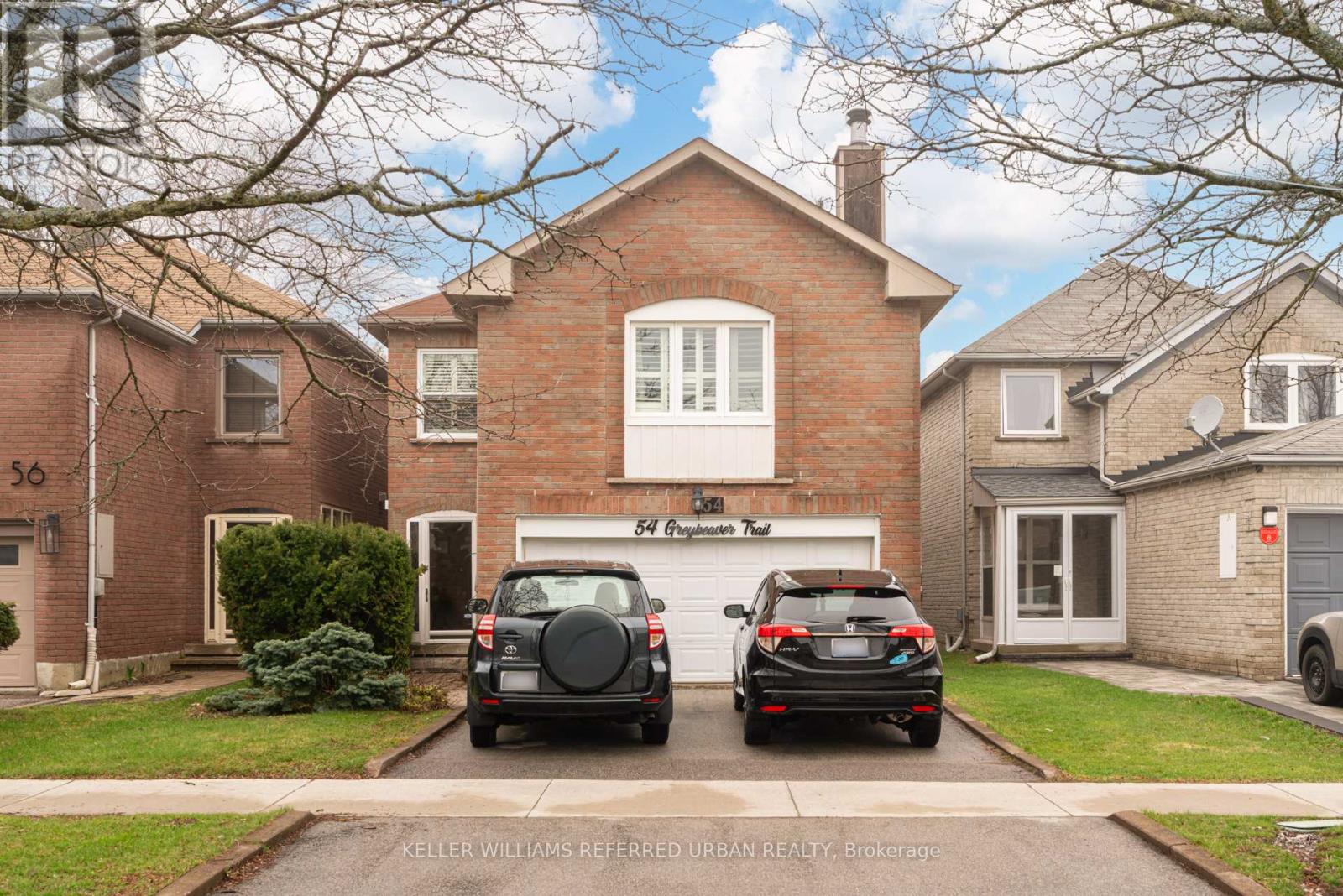 Two cars are parked in front of a brick house.