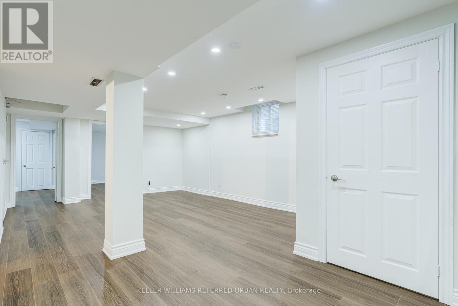 A spacious room with white walls and wooden flooring.