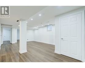 A spacious room with white walls and wooden flooring.